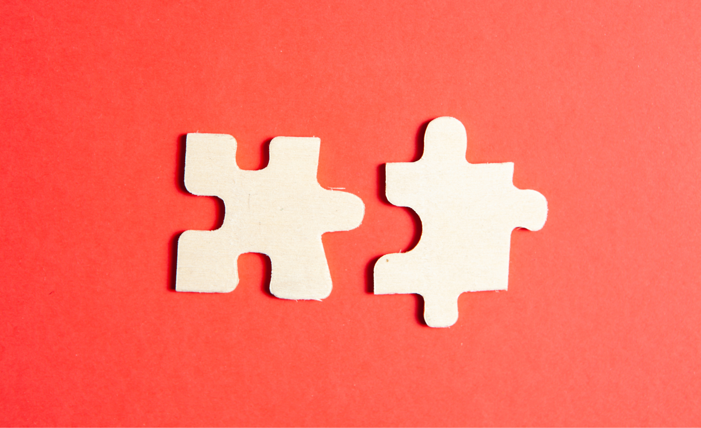 Two white puzzle pieces on a red background to symbolize the unification of two different content operations after a merger and acquisition.