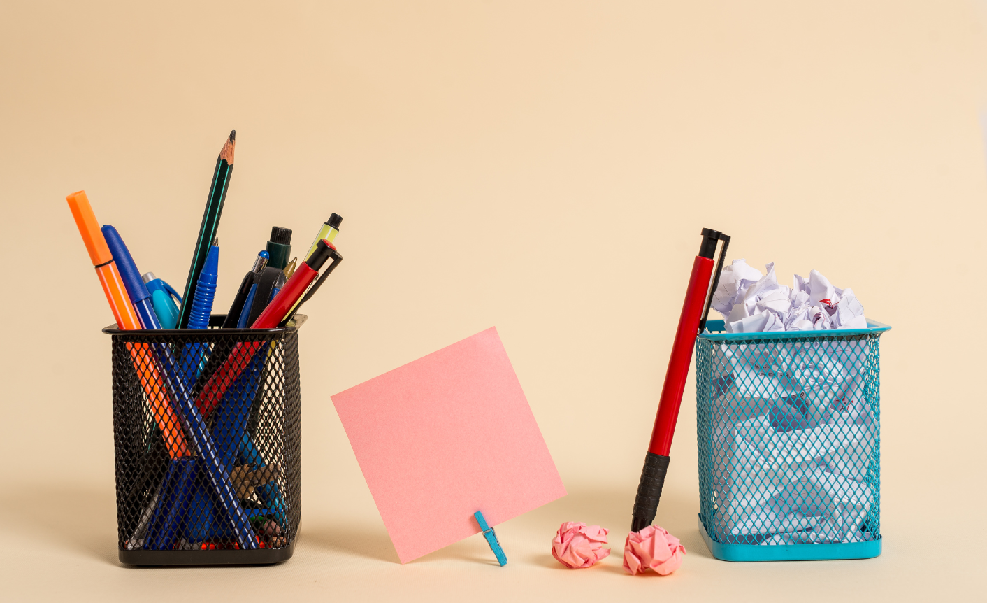 On a beige background, there are two wire baskets either side of a pink post-it note. The basket on the left is filled with pens and pencils and the basket on the right is filled with scrunched up paper. This is meant to symbolize that a lot of people create content at an enteprise.